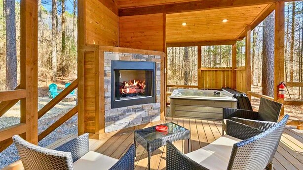 A wooden deck with a stone fireplace, outdoor seating, and a hot tub.