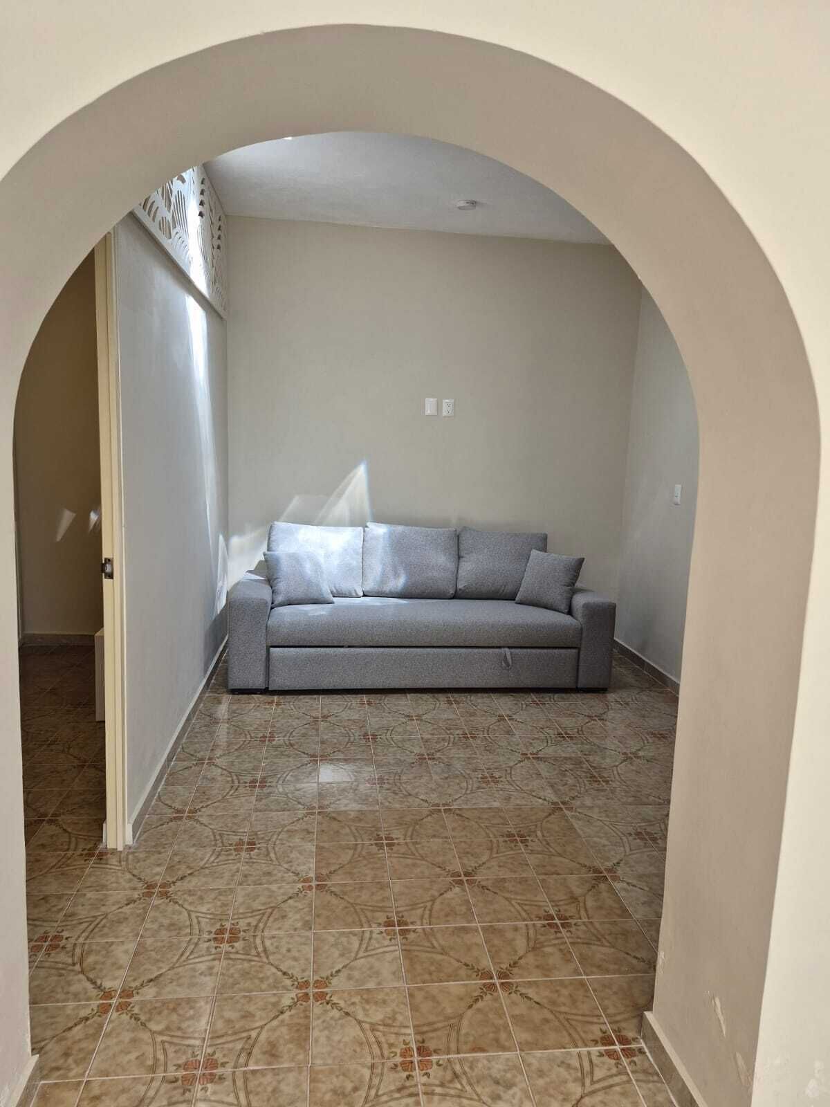 Una sala de estar con un sofá gris, baldosas de suelo estampadas y un arco blanco.