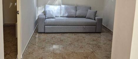 Una sala de estar con un sofá gris, baldosas de suelo estampadas y un arco blanco.