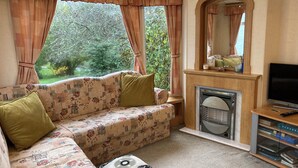 A cozy living room with a sofa, a fireplace, a television, and a bookshelf. - Charming 2-bedroom caravan in beautiful Clashmore with WiFi (Clashmore)