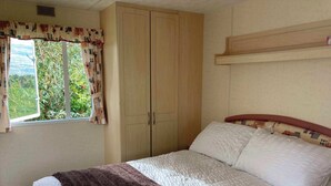 A bedroom with a bed, a wardrobe, a window with curtains, and a view of greenery outside. - Charming 2-bedroom caravan in beautiful Clashmore with WiFi (Clashmore)