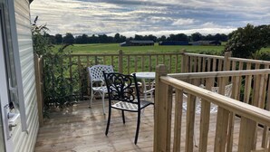 A wooden deck with a white chair and a table, overlooking a green field and distant buildings. - Charming 2-bedroom caravan in beautiful Clashmore with WiFi (Clashmore)