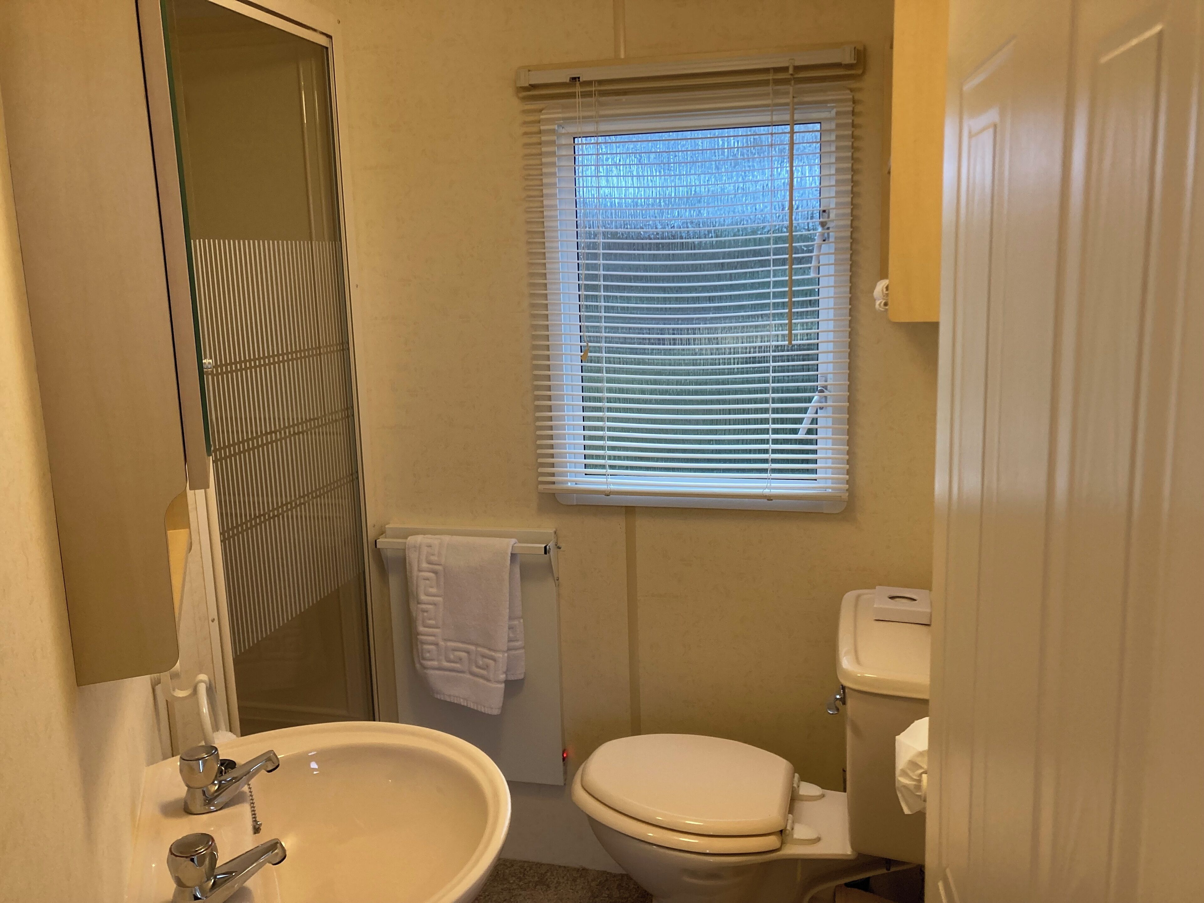 A bathroom with a sink, toilet, and window with blinds.
