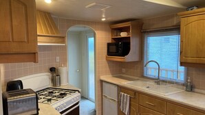 A compact kitchen with a gas stove, a toaster, a microwave, and wooden cabinets. - Charming 2-bedroom caravan in beautiful Clashmore with WiFi (Clashmore)