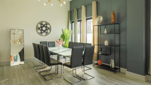 Une salle de réunion moderne avec une table en verre, des chaises noires, un lustre et un grand miroir.