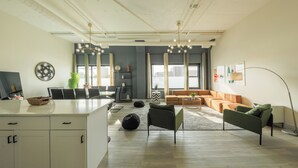 Un salon moderne avec un îlot de cuisine blanc, un canapé gris et un fauteuil en forme de sac noir.