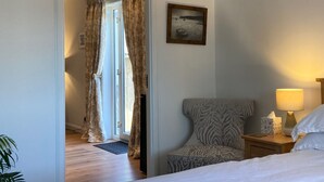 A hotel room with a bed, a nightstand with a lamp, a chair, and a door leading to another room. - Pet-friendly luxury garden apartment surrounded by woodland and fields. (Clashmore)