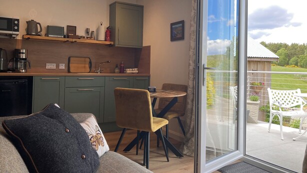 A modern kitchen with a dining area, a sofa, and a sliding glass door leading to an outdoor patio. - Pet-friendly luxury garden apartment surrounded by woodland and fields. (Clashmore)