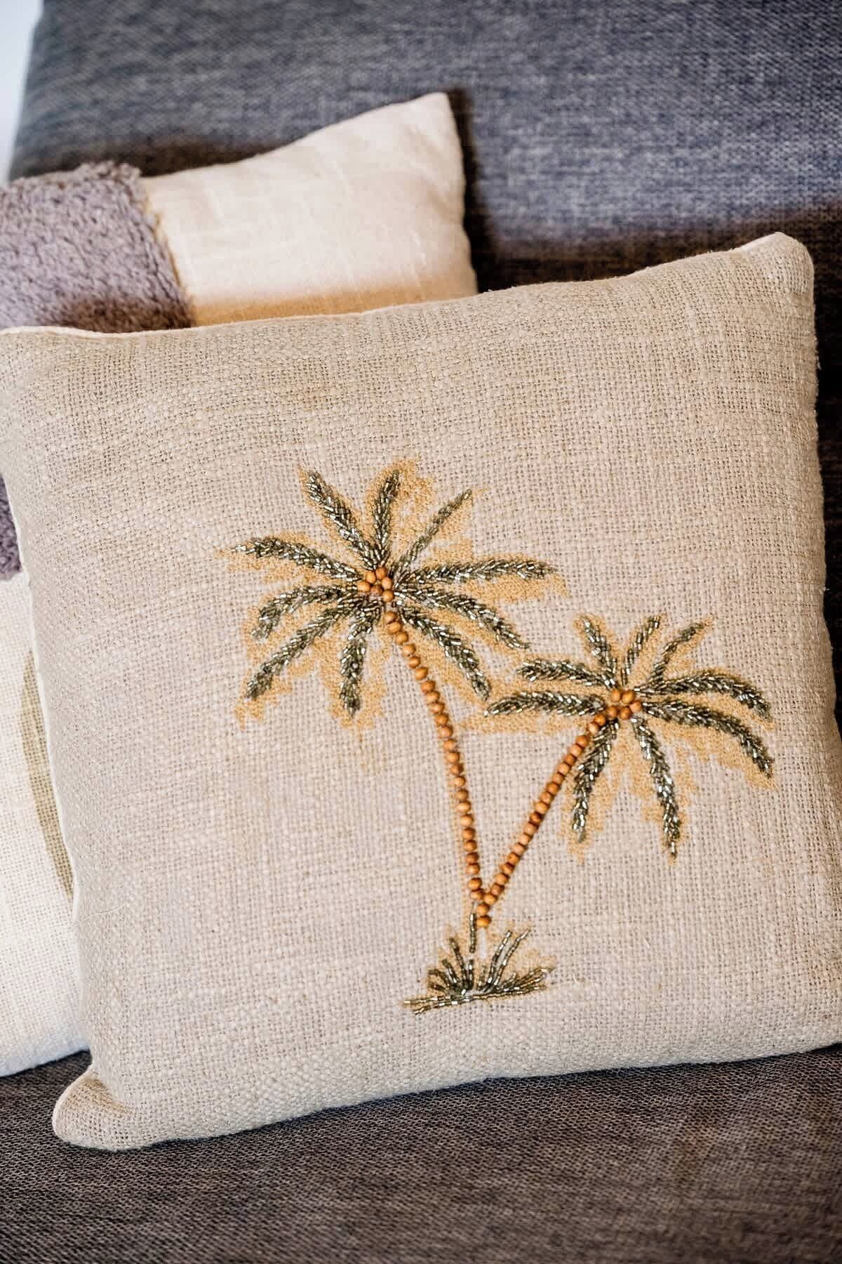 A beige pillow with embroidered palm trees on a dark gray couch.