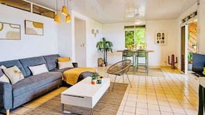 A modern living room with a grey sofa, a white coffee table, and a dining area with a green chair and table.