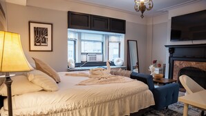 Une chambre bien éclairée, dotée d’un grand lit, d’un bureau, d’une chaise, d’une cheminée et d’un téléviseur fixé au mur.