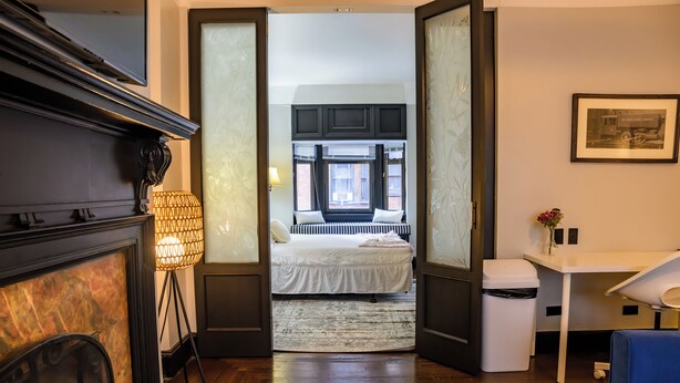 Une chambre à coucher comprenant un lit, un bureau, une chaise, une lampe et une vue sur la rue par une fenêtre.