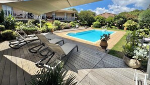 Eine Holzterrasse mit Schwimmbecken, Liegestühlen und einem schattigen Bereich.