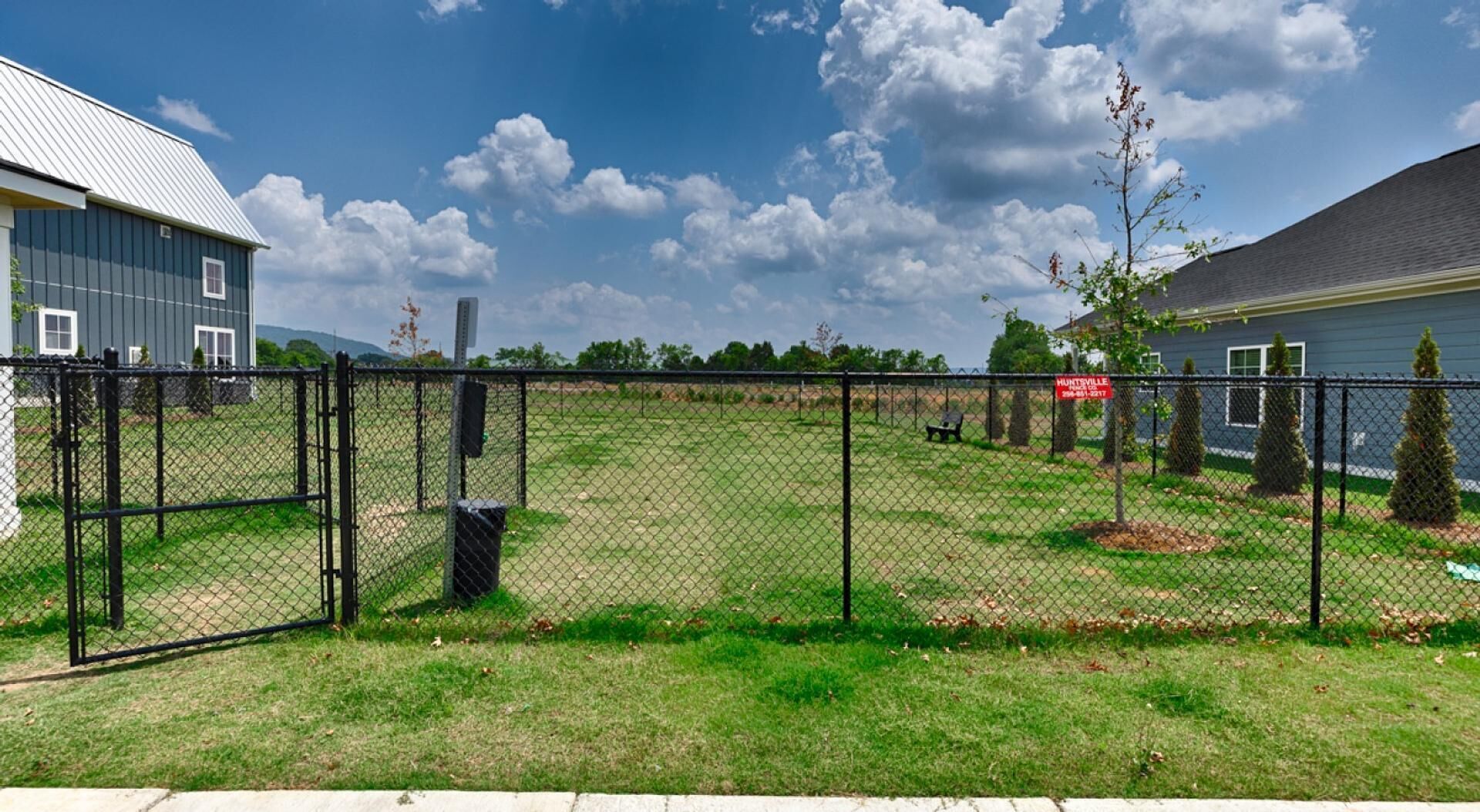 A fenced yard with a grassy area, a bench, and a sign indicating a location.