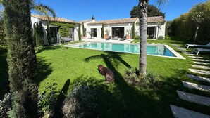 Una casa con piscina, césped y un perro.