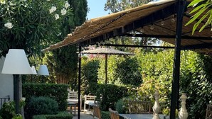 Un patio al aire libre con un pérgola, sillas de mimbre, una mesa de comedor y una lámpara.