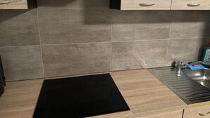 Una cocina con tope de inducción negro, un lavamanos de acero inoxidable y armarios de madera.