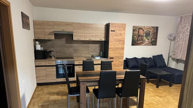 Una cocina compacta con armarios de madera, una mesa de comedor con sillas y un sofá de color oscuro.