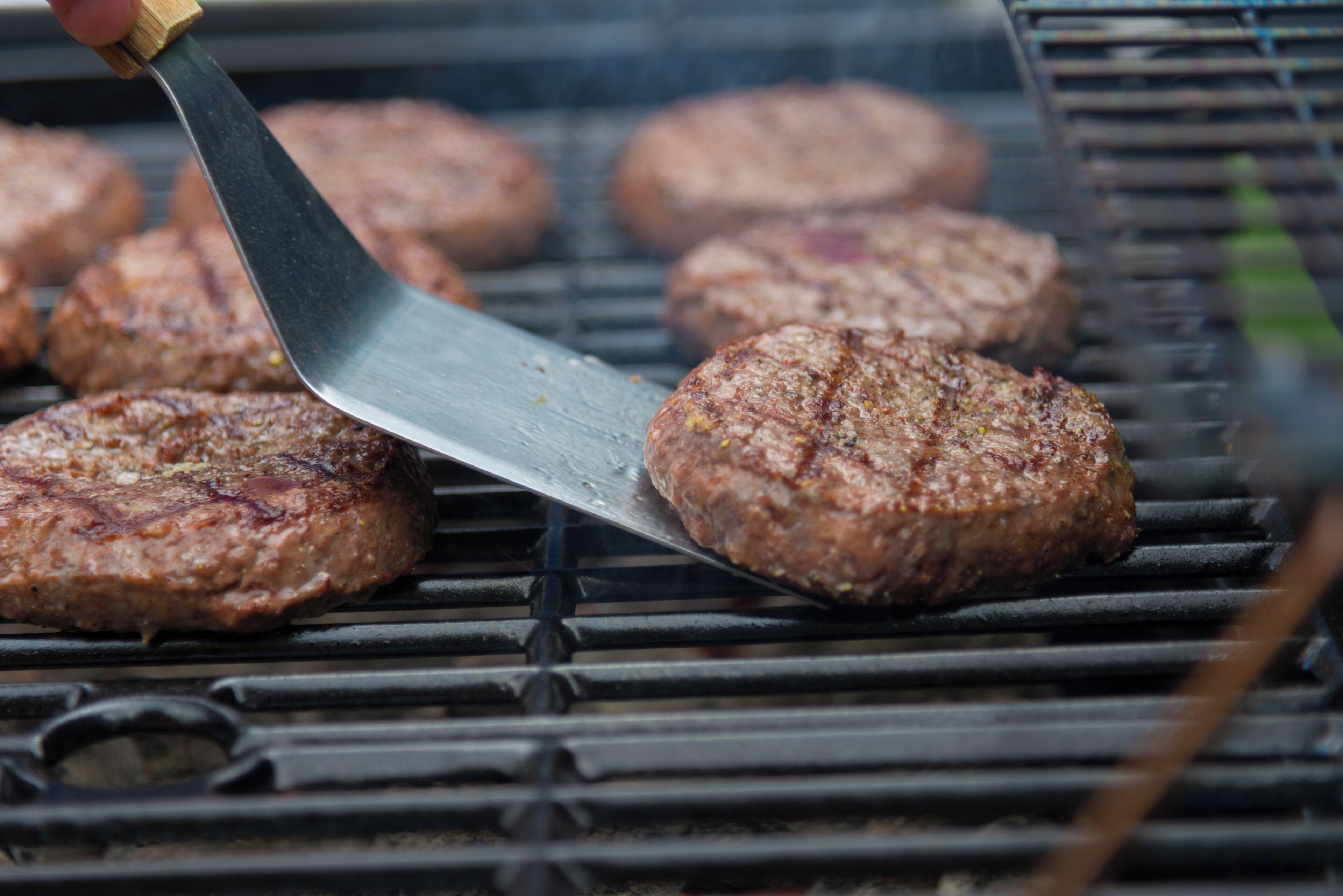 A close-up of hamburgers being grilled on a grill with a spatula.