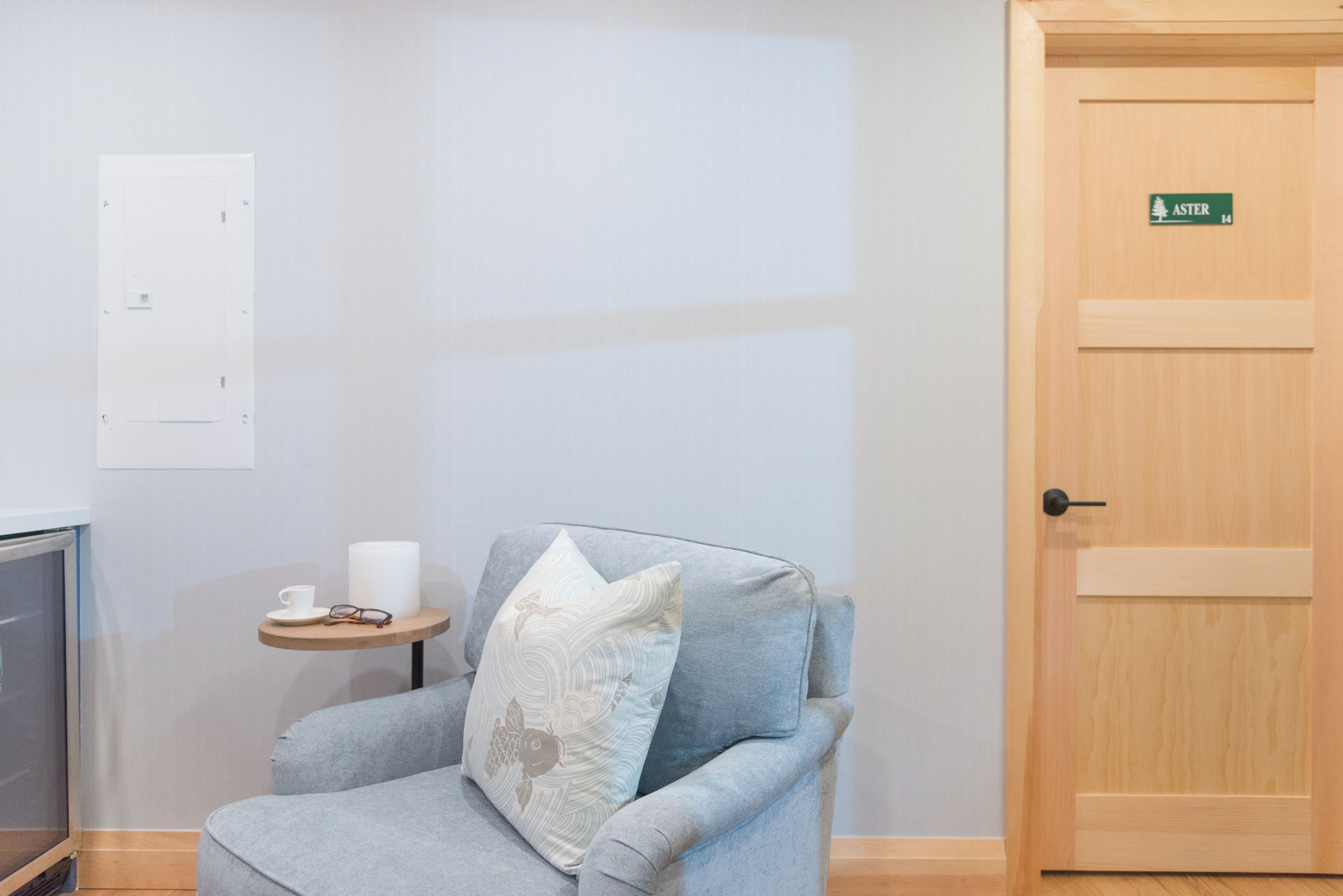 A room with a grey armchair, a small round table with a cup and glasses, a whiteboard, and a door labeled "ASTER 14".