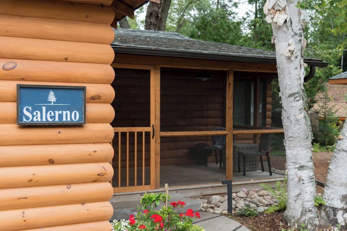 A log cabin with a sign reading "Salerno" and a covered porch with chairs.