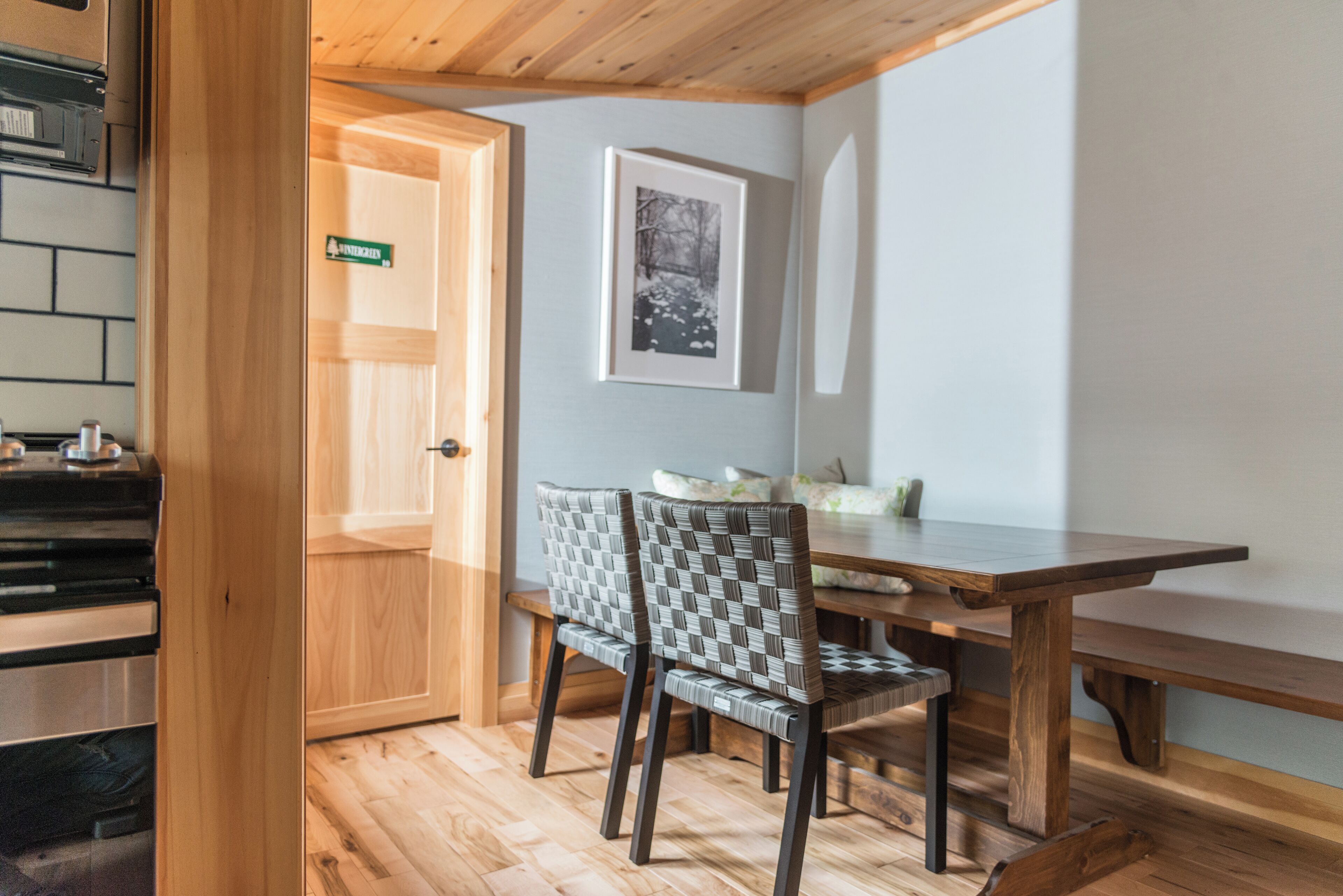 Ein Holztisch mit zwei Stühlen, ein gerahmtes Bild an der Wand und eine Tür mit einem grünen Schild.