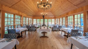 A spacious dining area with wooden walls and ceiling, large windows, and multiple tables set for dining. - Haliburton Post House (Minden)