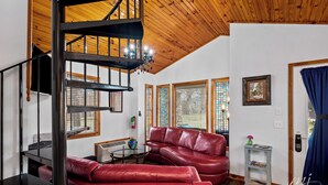 A spacious living area with a red leather sofa, a glass coffee table, and a wooden staircase. - Stunning 2 Bedroom Cabin In The Woods, Covered Porch, Jacuzzi, Kitchen & Hot Tub (Eureka Springs)