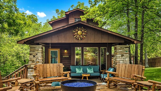 A rustic cabin with a stone fireplace, wooden furniture, and a stone exterior. - Stunning 2 Bedroom Cabin In The Woods, Covered Porch, Jacuzzi, Kitchen & Hot Tub (Eureka Springs)
