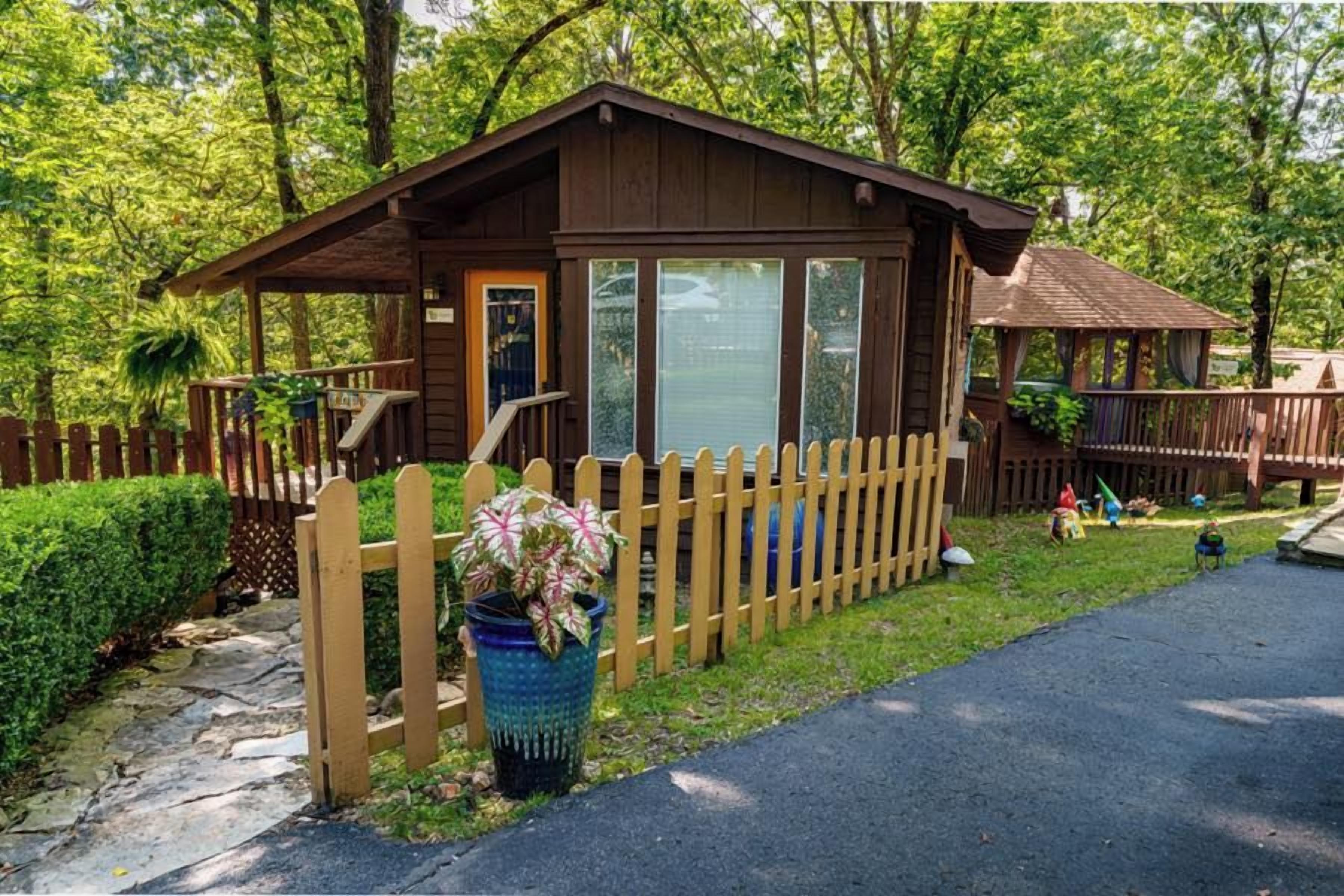 Eine Holzhütte mit Veranda, umgeben von einem Holzzaun, und ein Blumentopf im Vordergrund.