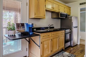 Une cuisine compacte avec des meubles en bois, un four à micro-ondes encastré, un réfrigérateur en acier inoxydable et une machine à café Keurig posée sur le plan de travail.