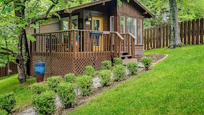 A cabin with a wooden deck, a small porch, and a fenced yard. - 1 Bedroom Cabin In The Woods, Covered Porch, Jacuzzi, Kitchen & Hot Tub. (Eureka Springs)
