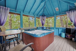 Un espacio exterior techado con jacuzzi, asientos y televisor.