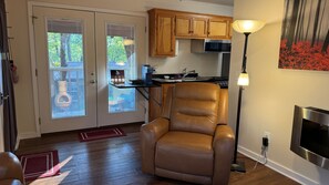 Una habitación con un sillón reclinable de cuero, una cocina con armarios de madera, estufa y televisor instalado en la pared.