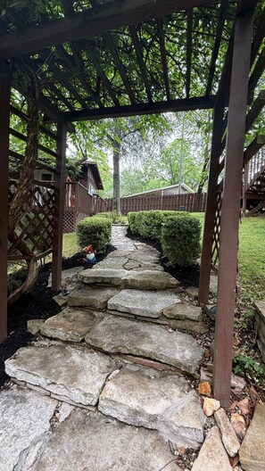 A stone pathway leading to a wooden pergola with a view of a residential area.