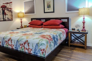 Una cama bien hecha con colcha floral, dos lámparas de noche y un cuadro enmarcado en la pared.