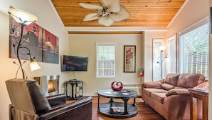 A living room with a fireplace, leather sofas, a round coffee table, and artwork on the walls. - 1 Bedroom Cabin In The Woods, Covered Porch, Jacuzzi, Kitchen & Hot Tub. (Eureka Springs)