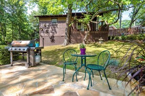A backyard with a stone patio, a barbecue grill, and a small table with chairs.