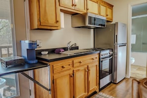 Una cocina compacta con armarios de madera, microondas integrado, estufa y refrigerador.