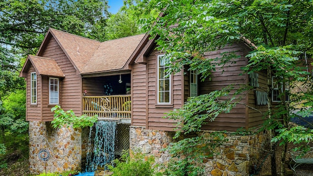 Une cabane en bois avec des fondations en pierre, une petite cascade et une terrasse en bois.