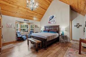 Un dormitorio amplio con una cama grande, techo de madera y vistas al exterior a través de una ventana.