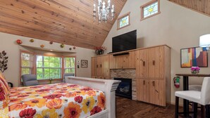 A bedroom with a large bed, wooden ceiling, a fireplace, and a TV. - 1 Bedroom Cabin In The Woods, Covered Porch, Jacuzzi, Kitchenette and Hot Tub. (Eureka Springs)