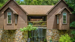 A wooden cabin with a stone foundation, a small waterfall, and a wooden deck. - 1 Bedroom Cabin In The Woods, Covered Porch, Jacuzzi, Kitchenette and Hot Tub. (Eureka Springs)