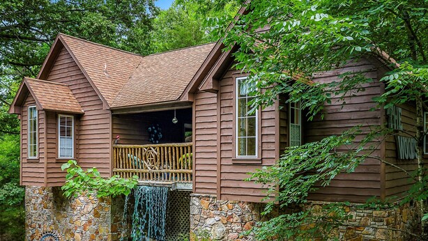 A wooden cabin with a stone foundation, a wooden balcony, and a waterfall feature. - 1 Bedroom Cabin In The Woods, Covered Porch, Jacuzzi, Kitchenette and Hot Tub. (Eureka Springs)