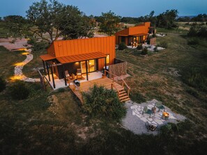 Uma casa moderna de dois andares com varanda e área de estar ao ar livre, rodeada por paisagem natural.
