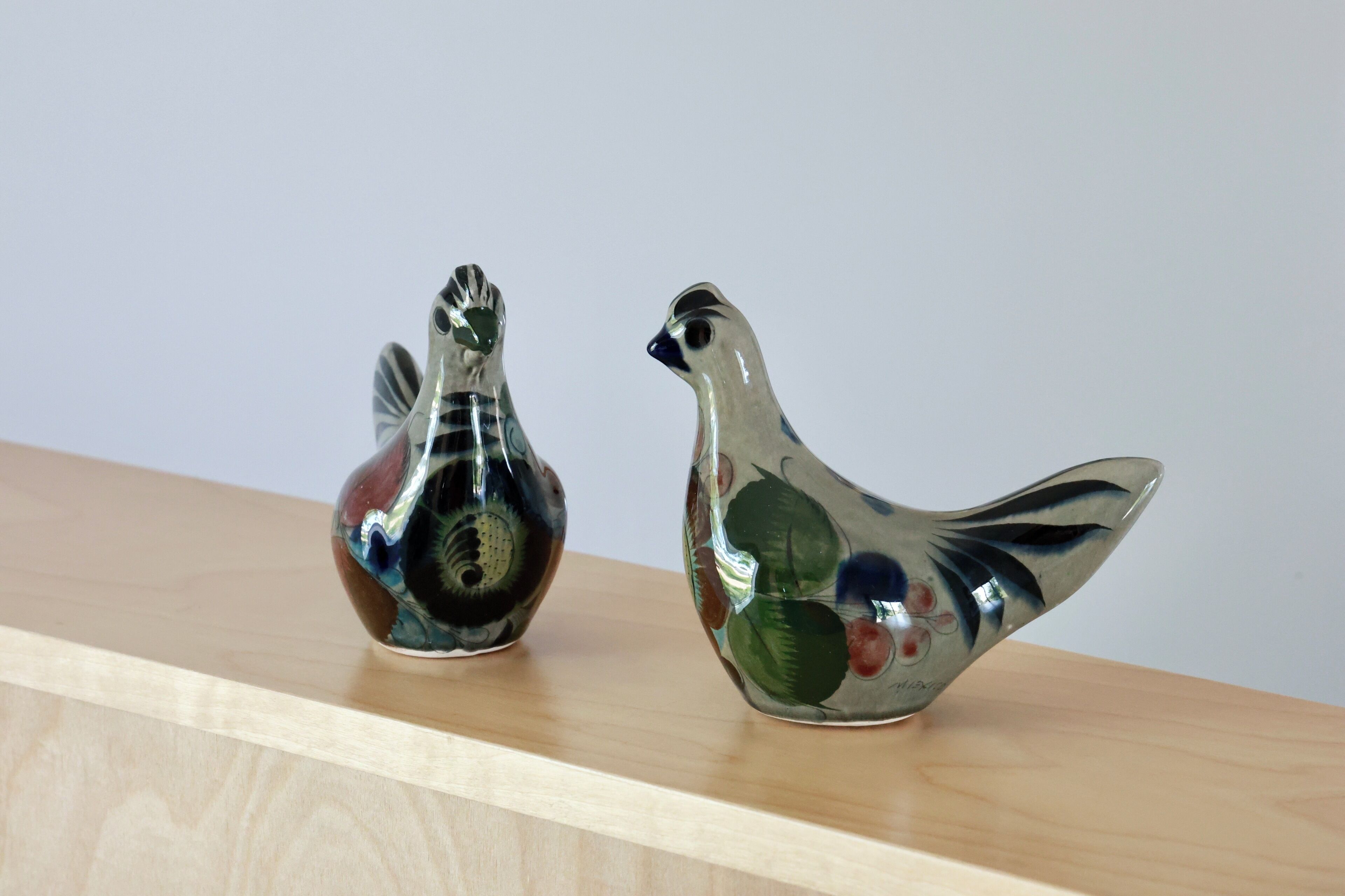Deux statuettes d’oiseaux en verre, posées sur une étagère en bois.