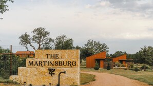 A sign for 'The Martinsburg' with a dirt path leading to buildings. - Luxury cabin in the center of the Texas Wine Country; large private porch w/hot tub, gas grill and fire pit; pet friendly (Stonewall)