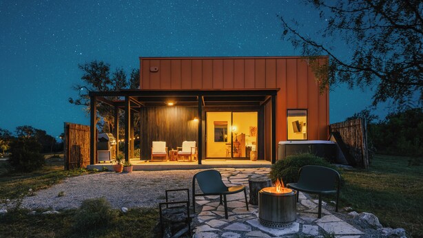 A modern house with a covered patio, stone pathway, and outdoor seating area with a fire pit. - Luxury cabin in the center of the Texas Wine Country; large private porch w/hot tub, gas grill and fire pit; pet friendly (Stonewall)