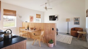 A modern kitchen with wooden cabinetry, a dining area with a table and chairs, a ceiling fan, and a living area with a sofa and a lamp. - Luxury cabin in the center of the Texas Wine Country; large private porch w/hot tub, gas grill and fire pit; pet friendly (Stonewall)
