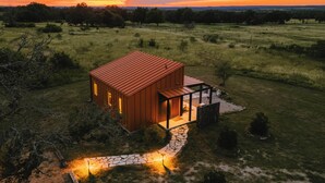 A modern house with a red roof, surrounded by a grassy field and trees. - Luxury cabin in the center of the Texas Wine Country; large private porch w/hot tub, gas grill and fire pit; pet friendly (Stonewall)